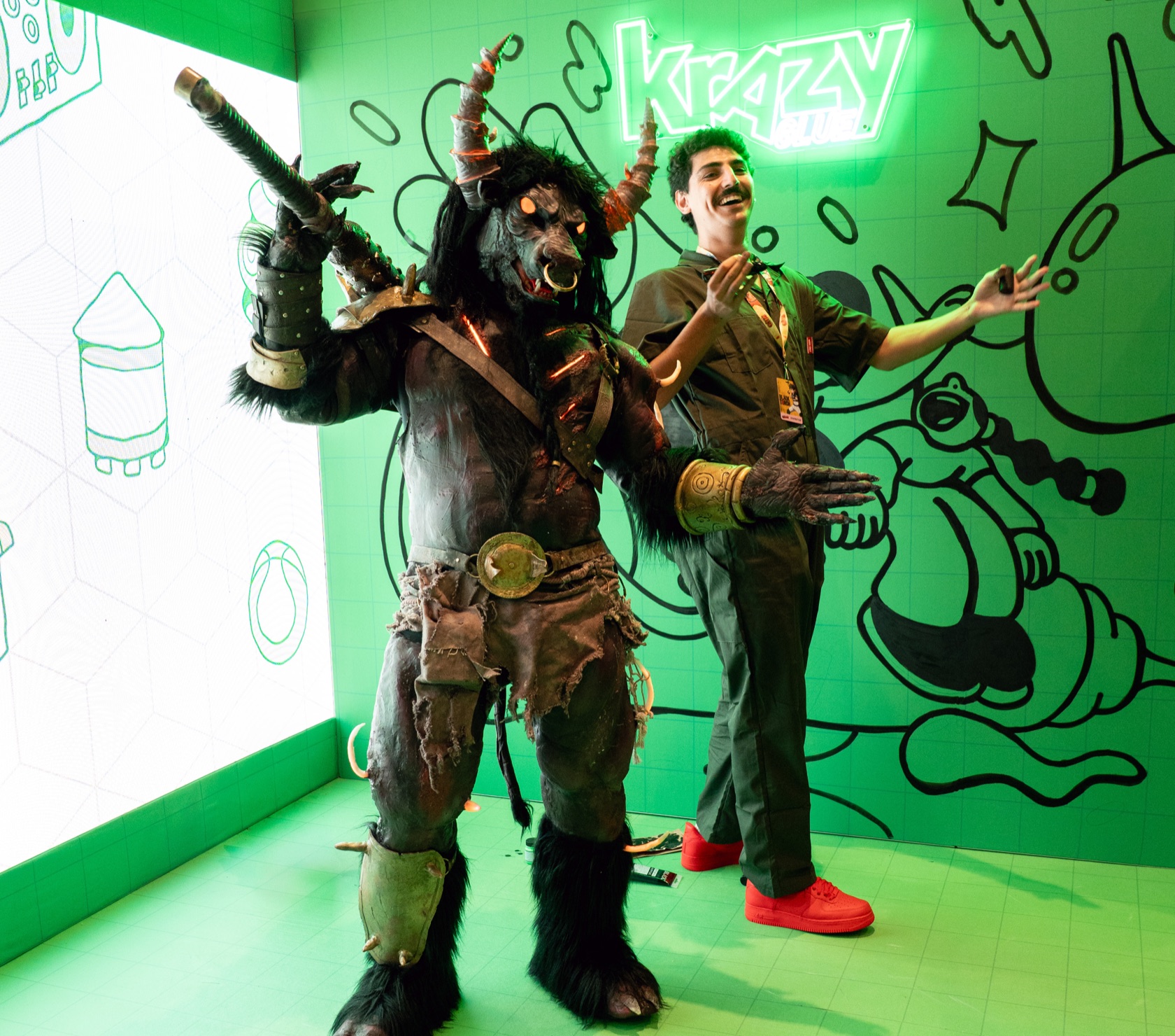 A horned cosplayer and a grinning guest under a Krazy Glue neon sign